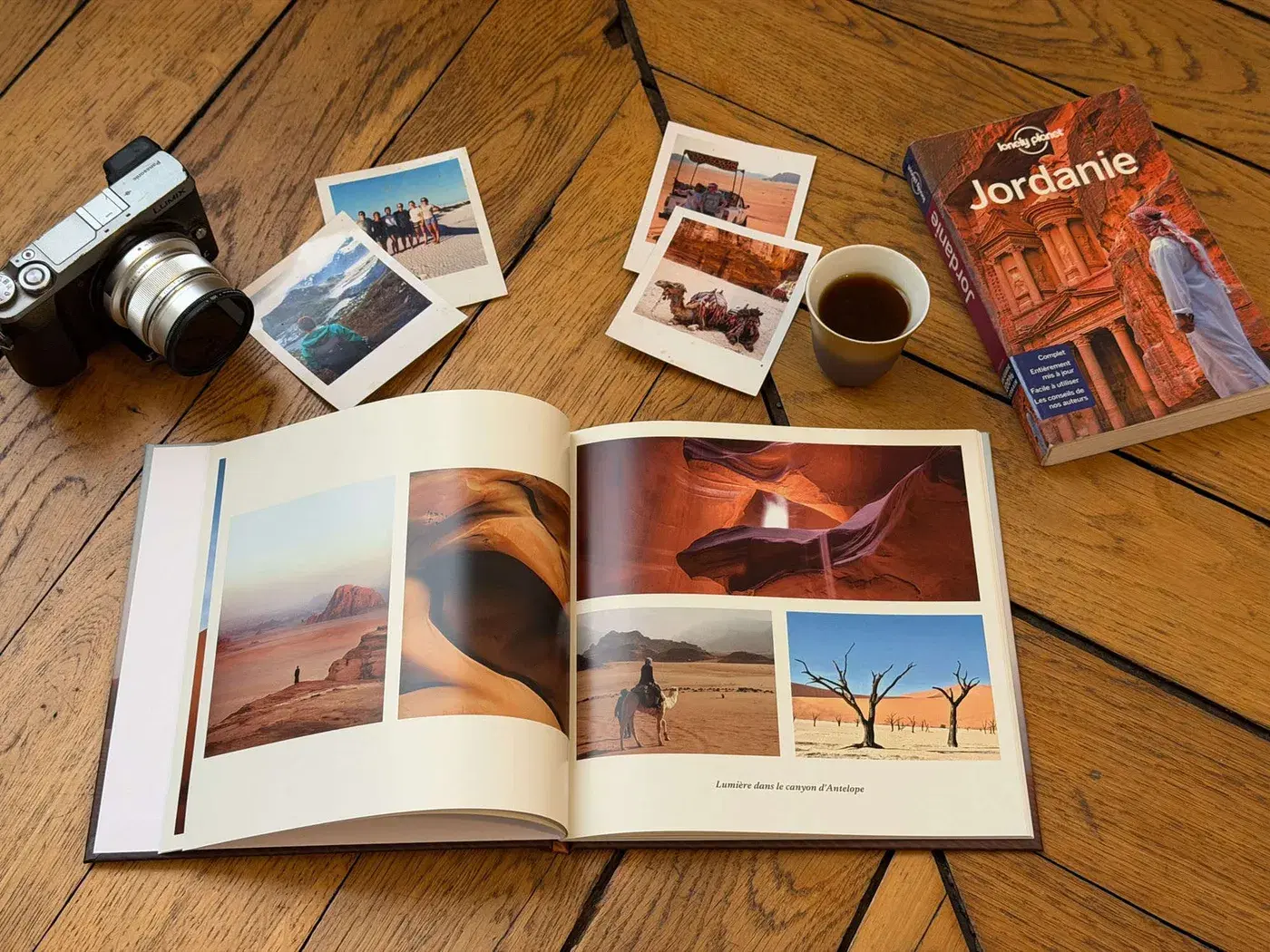 An open album lying on a wooden floor beside a camera, a few prints and a guidebook
